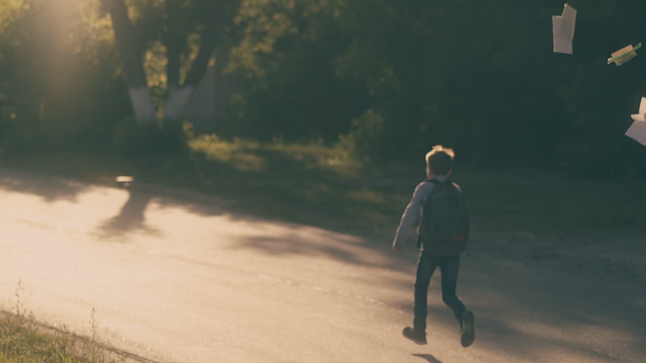청바지를 입은 행복한 학생이 도로를 따라 달리고 시트를 던집니다.