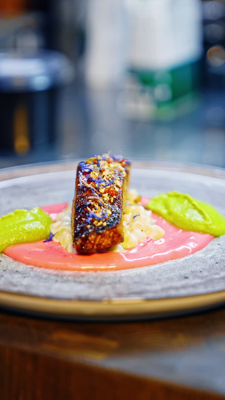 A piece of fish with two types of sauce on the rotating plate. Beautiful serving of a dish in the restaurant. Blurred backdrop. Close up. Vertical video.