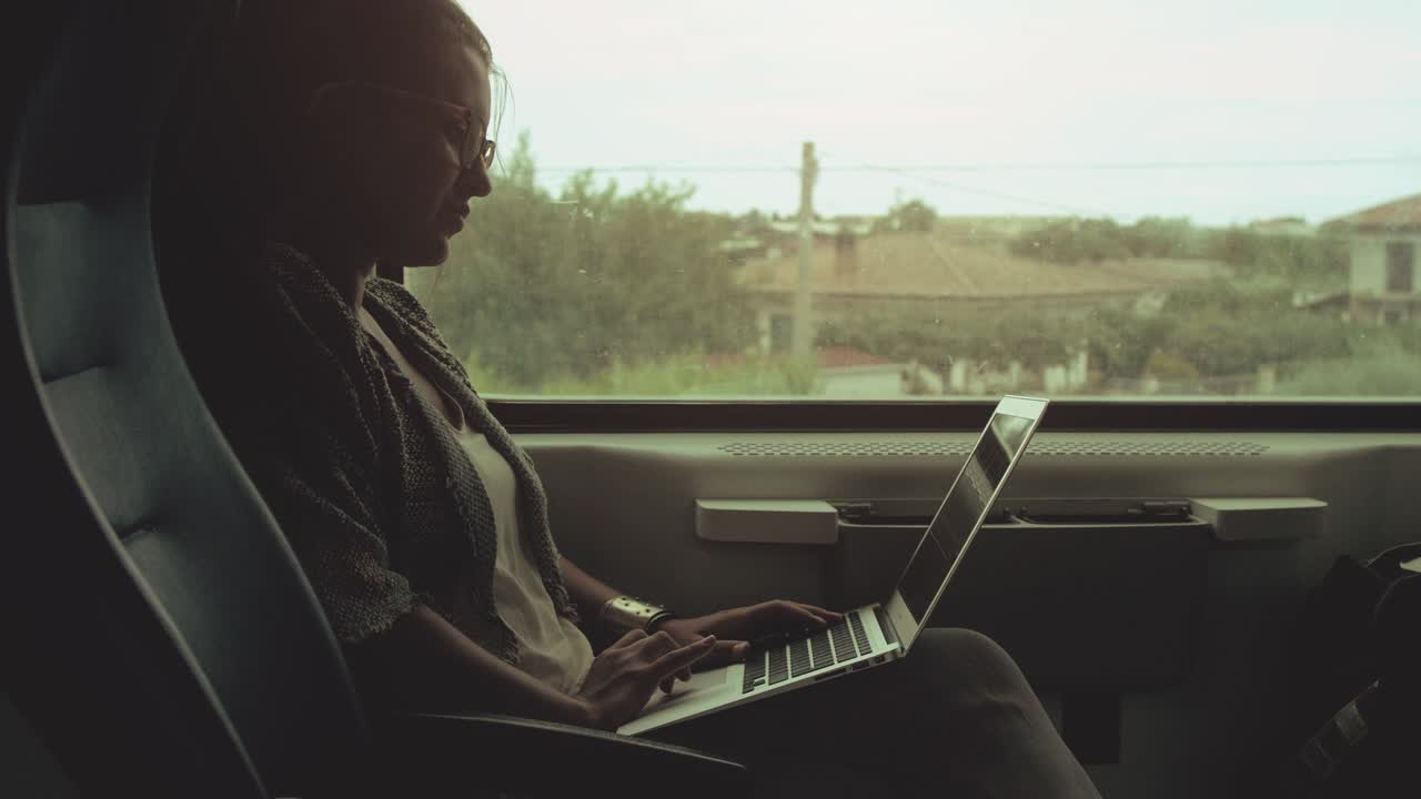 Young woman with glasses using laptop on moving train