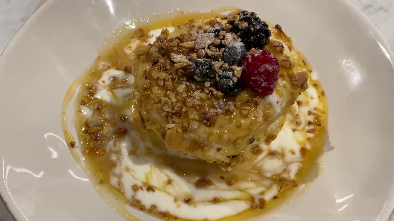 블루베리, 딸기, 크림을 곁들인 갓 구운 팬케이크에 꿀을 붓는다