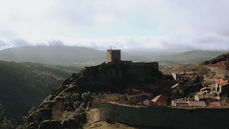 castillo medieval aislado en la cima de una colina detrás de los árboles, revelando una toma aérea