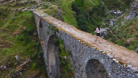 aerial of young girl crossing the ali pasha aqueduct bridge during trekking in the mountains