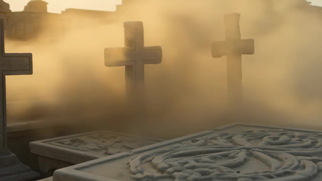 Nebbia in movimento sotto il sole caldo che rivela una grande croce di pietra centrale e una lastra tombale scolpita al cimitero.