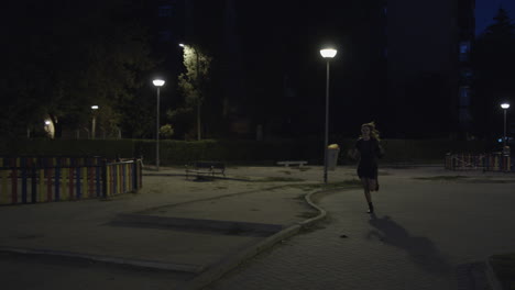 scared woman in black casual dress running away passing by an empty park with street lamps late at night in spain