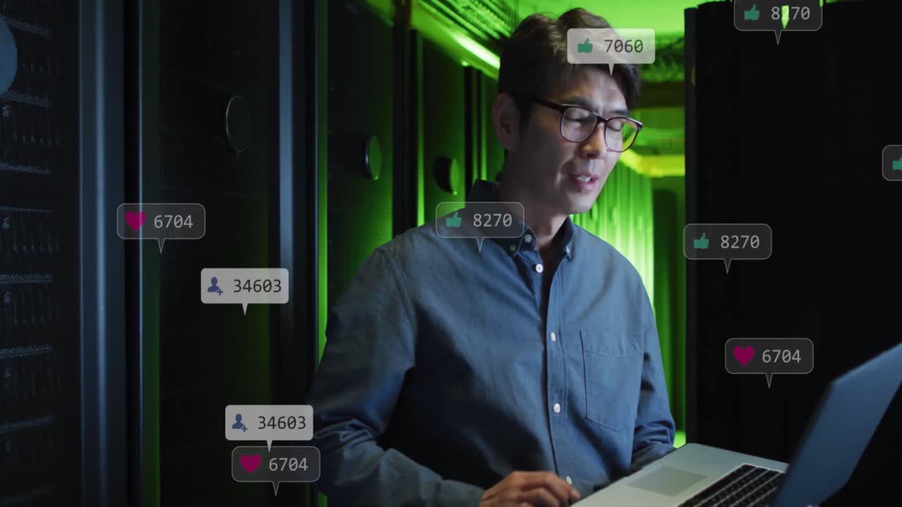 animación de iconos de las redes sociales contra un ingeniero asiático usando una computadora portátil en la sala de servidores de computadoras.