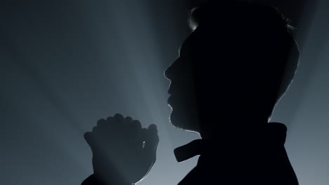 silhouette religious man asking god blessing. male person praying in darkness.