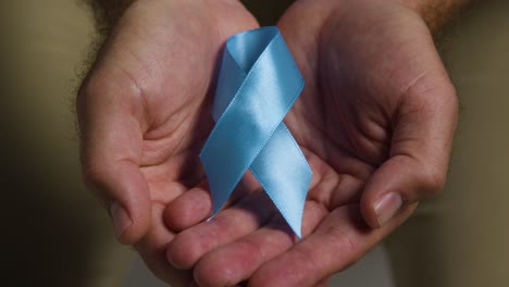 close up of person holding blue ribbon symbolizing awareness of men's health and cancer 2