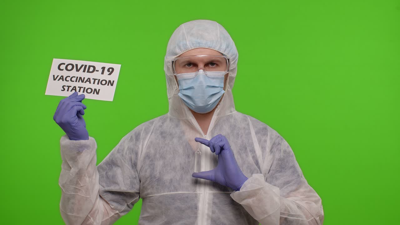 Medical doctor in PPE suit with medicine ampoule and text on paper - Covid-19 Vaccination Station