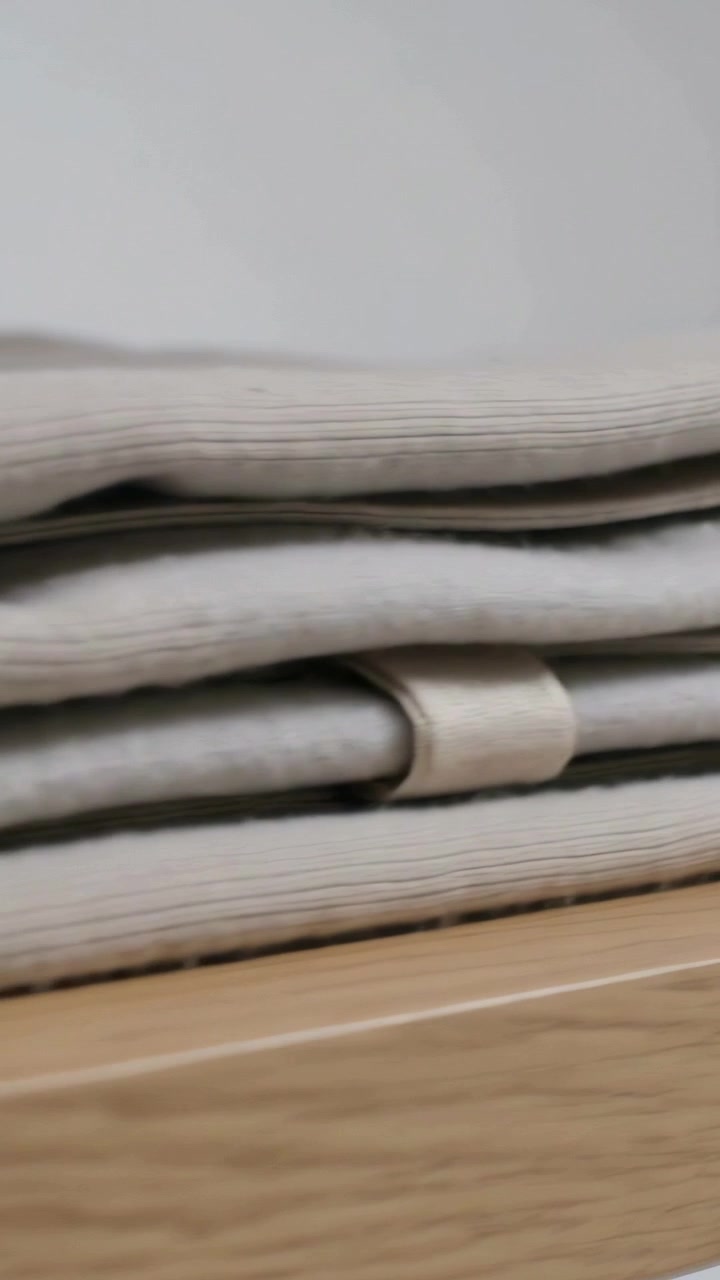 Vertical video: Camera panning closer revealing folded beige knit on wood table to show ribbed loop