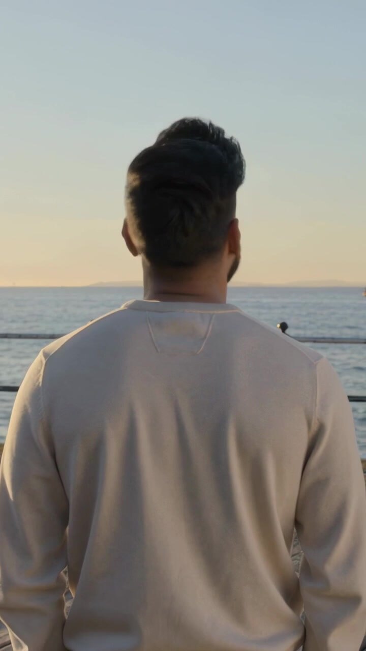 Vertical video: Standing man in light sweatshirt turning to friend pointing at boat on pier sunset