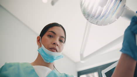 a female doctor or nurse wearing a face mask looks at the camera in a hospital or clinic setting.
