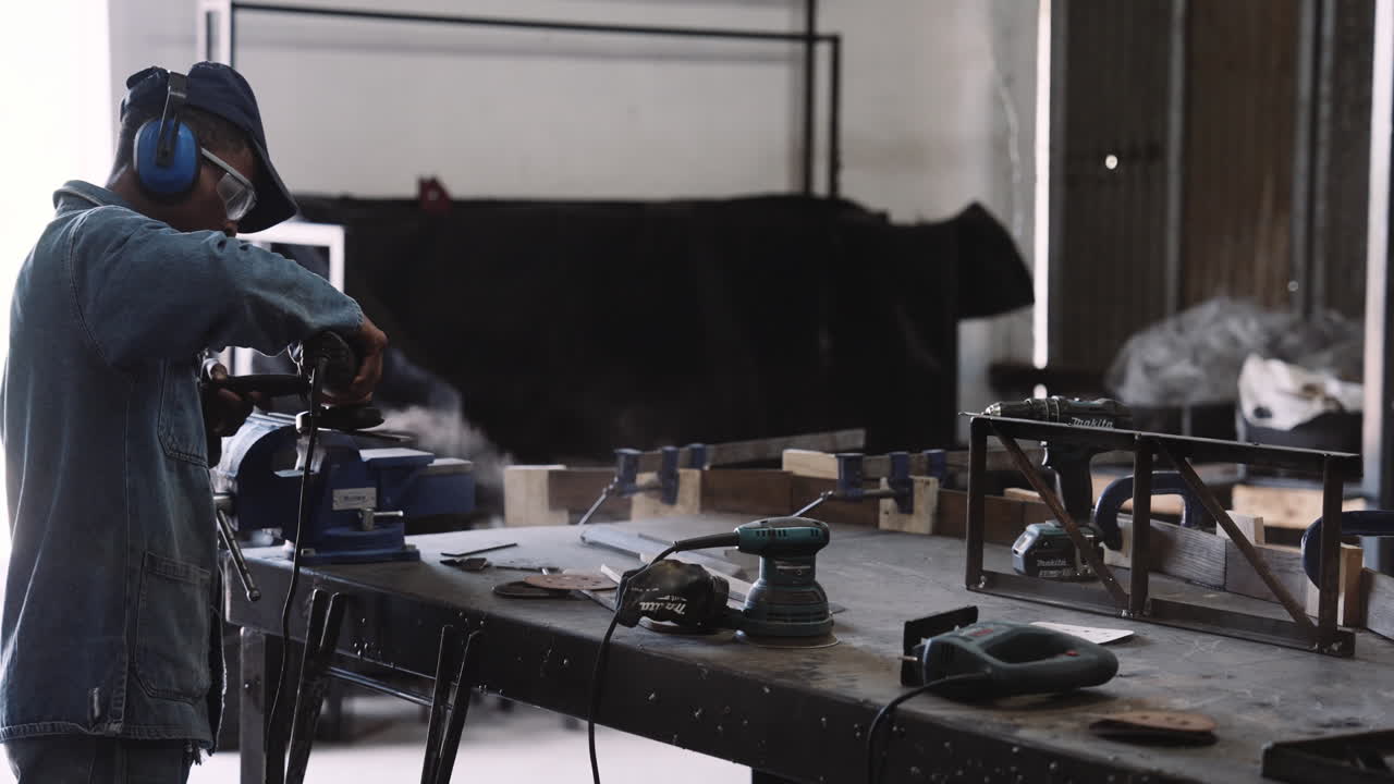 Slow motion track right of young black male working angle grinder power tool with sparks over workshop table