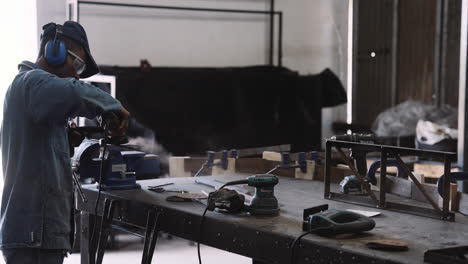 slow motion track right of young black male working angle grinder power tool with sparks over workshop table