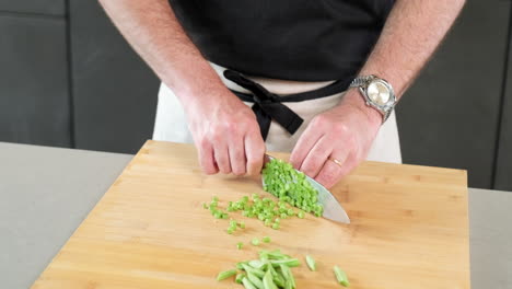 male chef slicing precisely the green bean with his knife on the cutting board at his kitchen