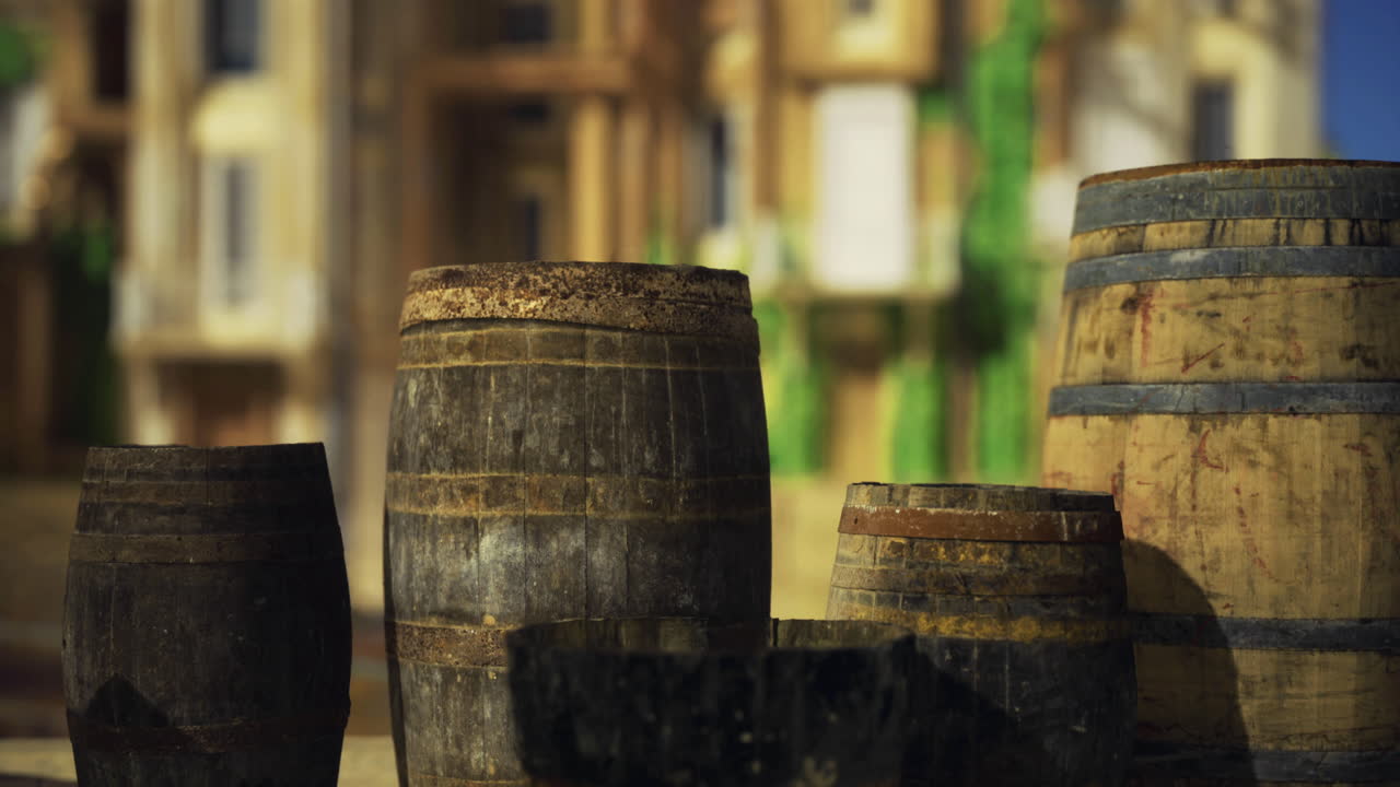 Barrels of various sizes placed outdoors in a sunny environment near buildings