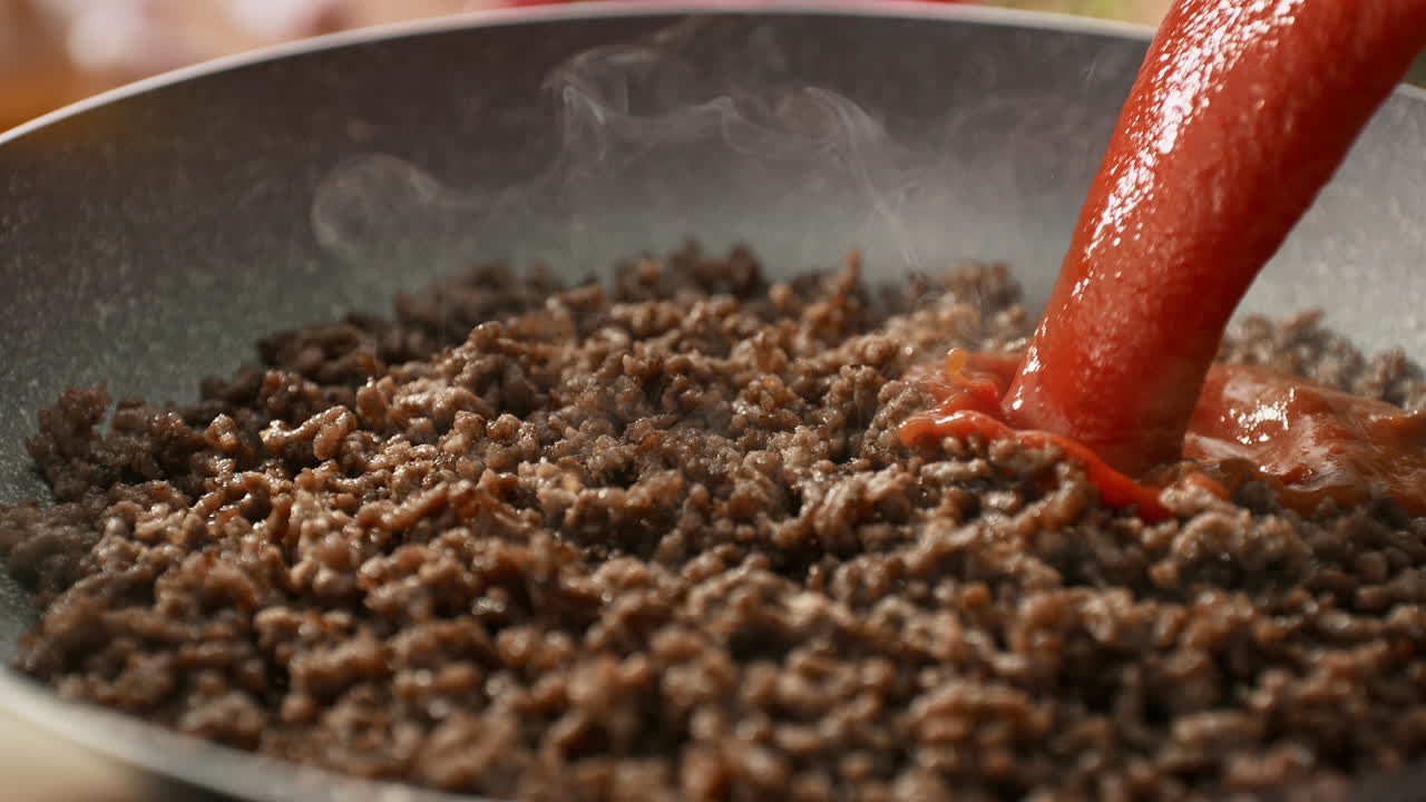 carne picada en una sartén con una corriente de salsa de tomate rojo derramada sobre ella en cámara lenta - cocinar espagueti bolognese en una cocina