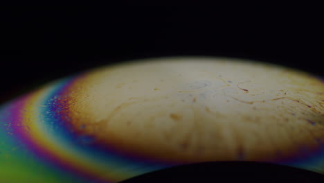 macro shot of a soap bubble with rainbow colored strips on the edge of the pole