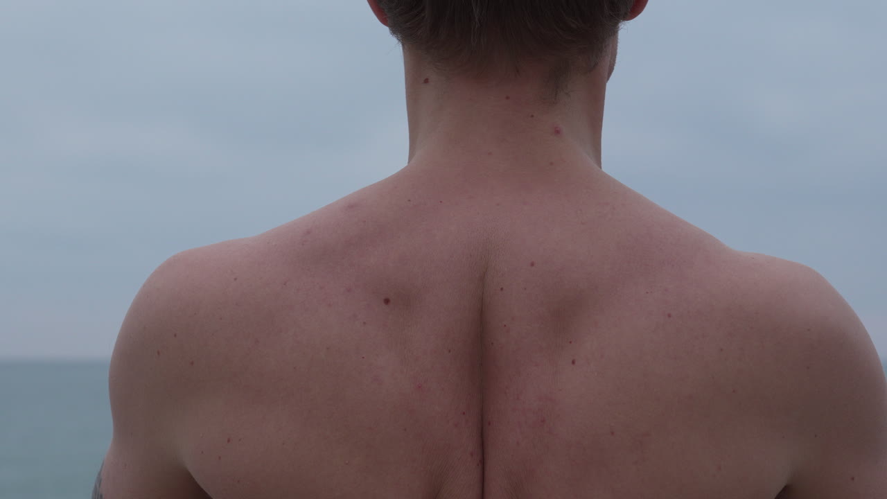 обнаженный мужчина медитирует, находясь в спокойном море, его мышцы напрягаются, когда он глубоко вдыхает и выдыхает, а в конце кланяется.