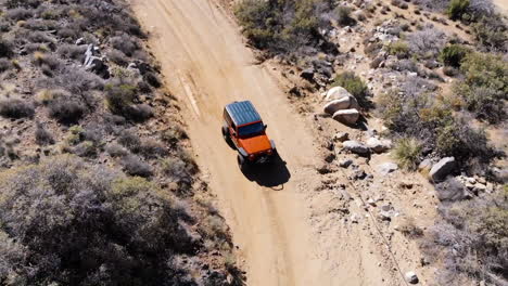 aerial of orange off road vehicle driving on dirt road through desert mountains - looking at front of vehicle