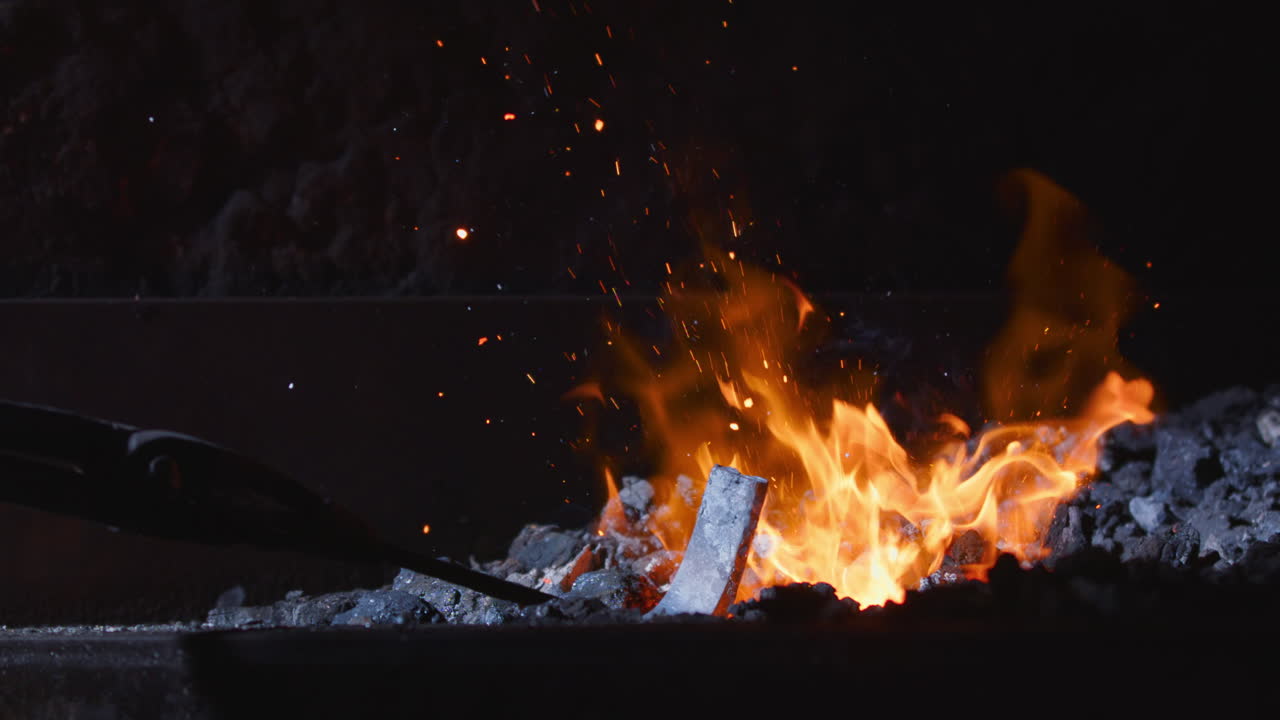 Embers rise as metal piece is inserted into swelteringly hot blacksmithing forge