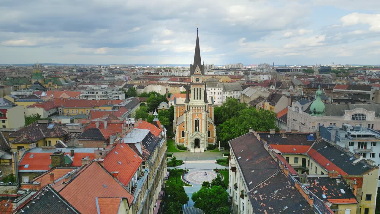 Wide aerial view of St. Francis of Assisi Parish, a neo-Romanesque Catholic church in Budapest, Hungary, surrounded by greenery and cityscape under an overcast sky.