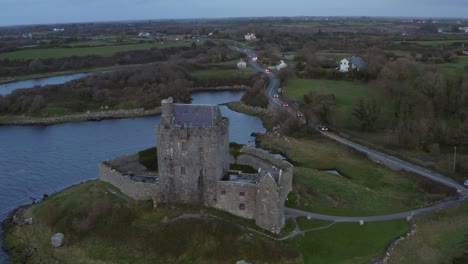 Cinematic-orbit-aerial-of-Dunguaire-Castle-and-the-coast-road-with-traffic-at-twilight