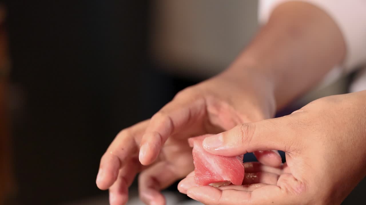 Close-up shot of a chef's hands skillfully pressing and shaping fresh tuna nigiri sushi