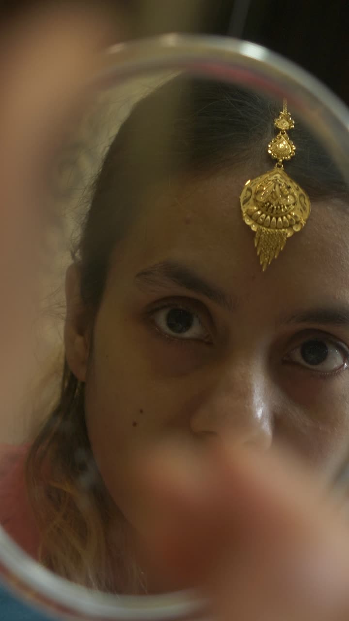 Young and beautiful south asian woman wearing gold jewellery while looking at mirror, Closeup, Vertical shot