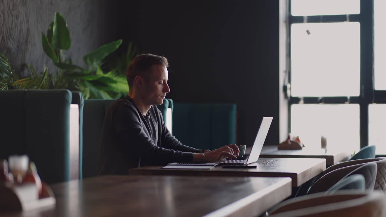 A serious man is a business student working studying sitting at a table and typing a message on a laptop. Typing text on the keyboard