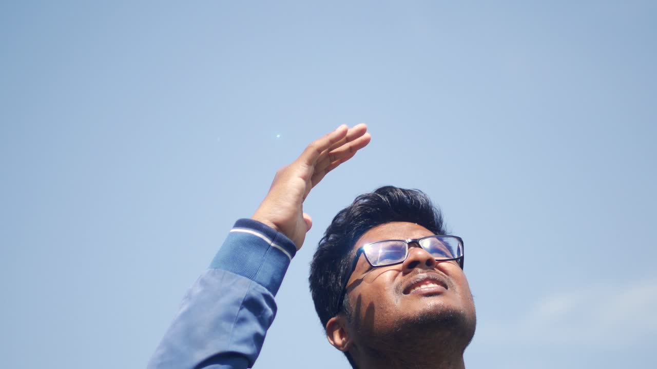 A man looking up at the sky, shielding his eyes from the sun with his hand