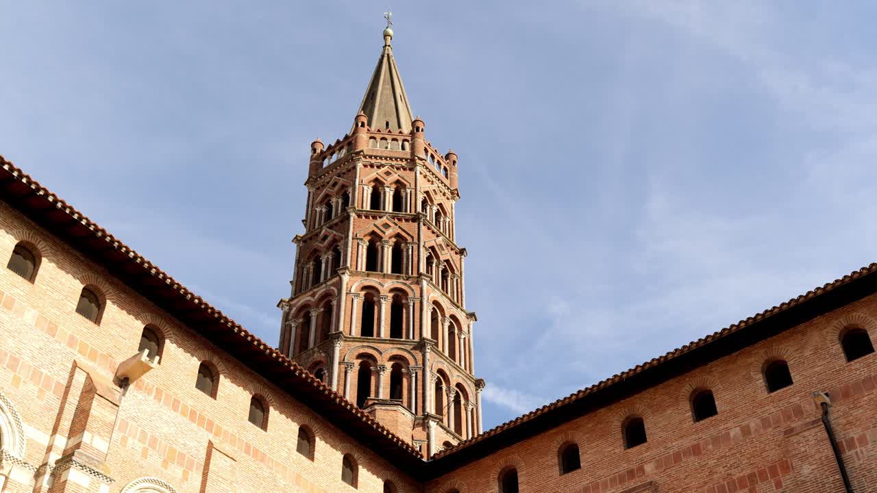 Vista dal cortile che guarda verso l'alto il magnifico campanile ottagonale della Basilica di Saint-Sernin a Tolosa con calde pareti in mattoni rosa che convergono in modo spettacolare sotto un cielo blu parzialmente nuvoloso