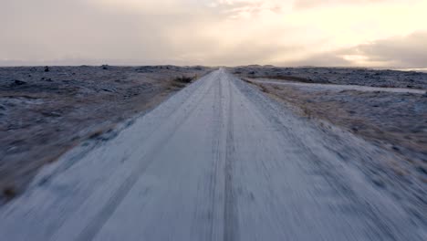 Ascending-aerial-shot-of-frozen-iced-Road-surrounded-by-snow-covered-lava-field-in-Iceland