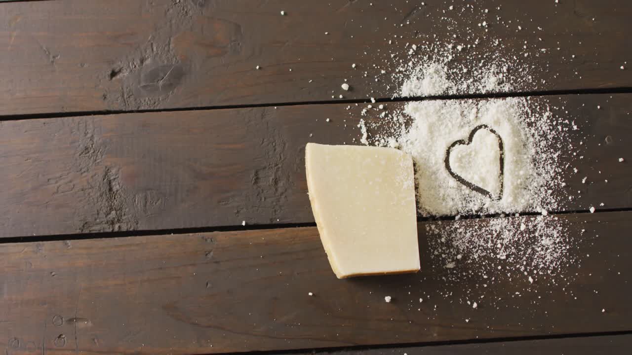 vídeo de un bloque de queso duro y un corazón dibujado en queso rallado en una mesa rústica con espacio para copiar