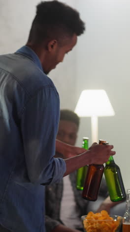 african-american guy carries bottles of cold beer to joyful friends watching sports game together. young fans group enjoys football match at home