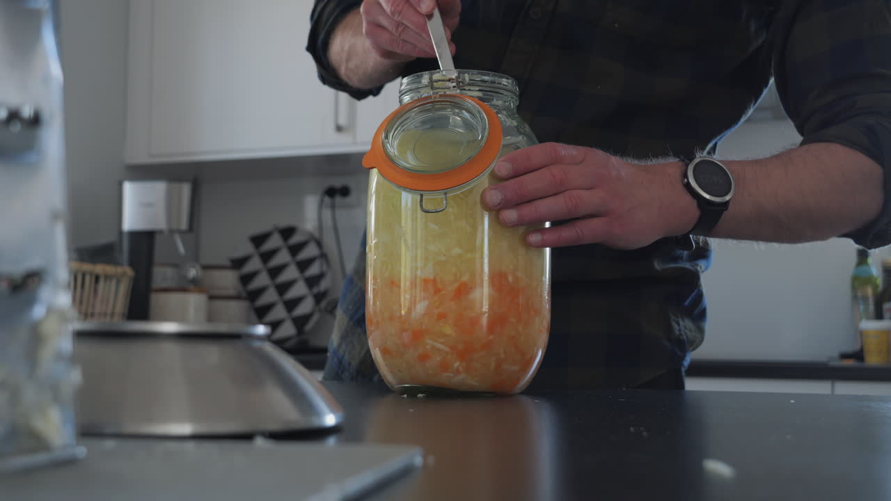 hombre presionando verduras fermentadas o chucrut en tarro, cerrar