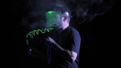 man smokes strange neon tube in clear face shield, tilt up isolated on black