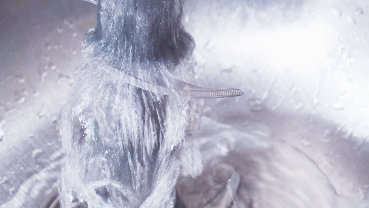 Washing a food processor blade under running water in a stainless steel sink