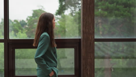 una mujer en un blazer verde de pie junto a una ventana mirando hacia lejos