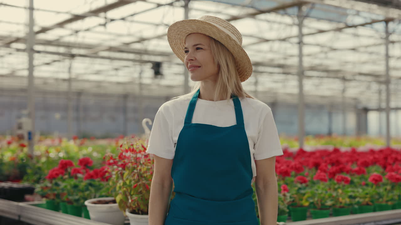 Smiling Woman Gardener in a Greenhouse with Red Flowers