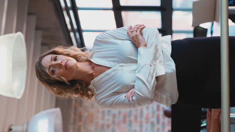 vertical video portrait of serious businesswoman in office with colleagues working in background