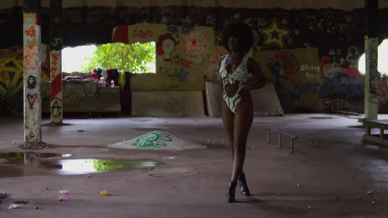 Studio quality shot: A Black female model wearing a bikini, sharply posed against the rugged, geometric background of an empty indoor skate park