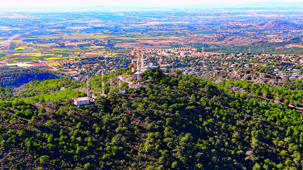 Antenne e tralicci per le telecomunicazioni situate su una collina boscosa e verdeggiante che domina una vasta pianura costiera. Torri di comunicazione sulla cima di una collina boscosa.