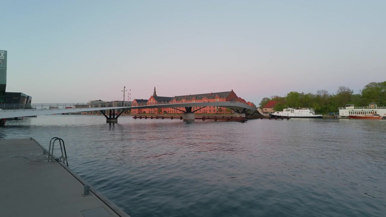 Città, fiume, tramonto, ponte, edifici, ripresa con stabilizzatore gimbal. Avanzamento cinematografico a 60fps camminando sulla riva di Copenaghen osservando biciclette sul cavalcavia e barche ormeggiate