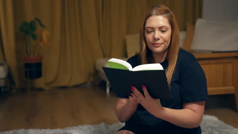 A-woman-reading-a-book-and-sitting-on-a-rugrelaxing-at-home-in-her-living-room