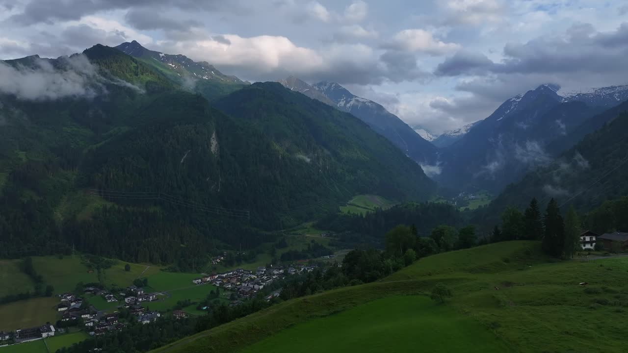Paesaggio montuoso e insediamento sottostante avvolti da nuvole e nebbia.