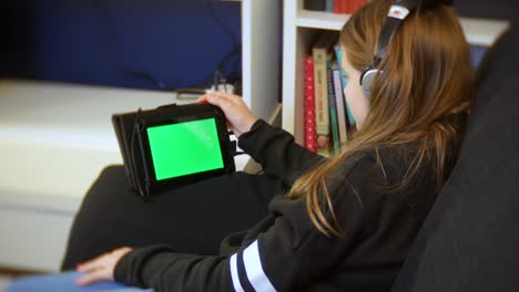 Young-girl-sits-at-home-using-her-tablet-with-her-headphones-on