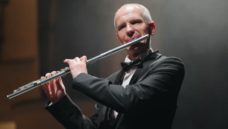 Flautista-De-Pelo-Gris-Está-Tocando-Música-Clásica-Con-Flauta-Retrato-De-Músico-En-La-Sala-Oscura-De-La-ópera