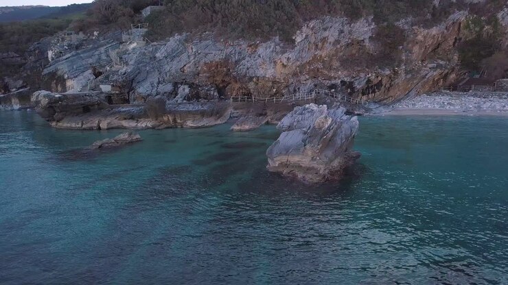 Ripresa aerea con drone in orbita antioraria di una grande roccia nelle acque cristalline del mare in Grecia