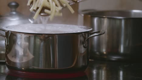 cooking and stirring ziti pasta using a wooden spatula on a stainless pot with boiling water and bubbles on top