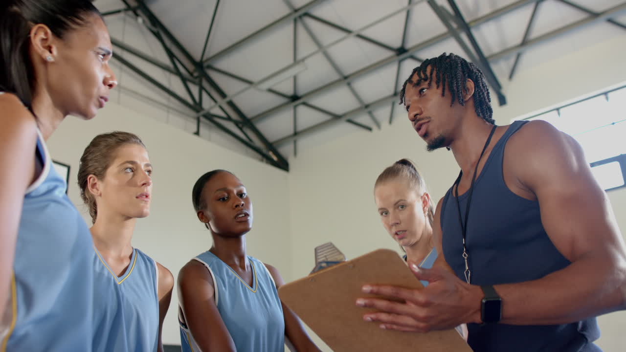 Basketball coach discussing strategy with female players in gym during practice